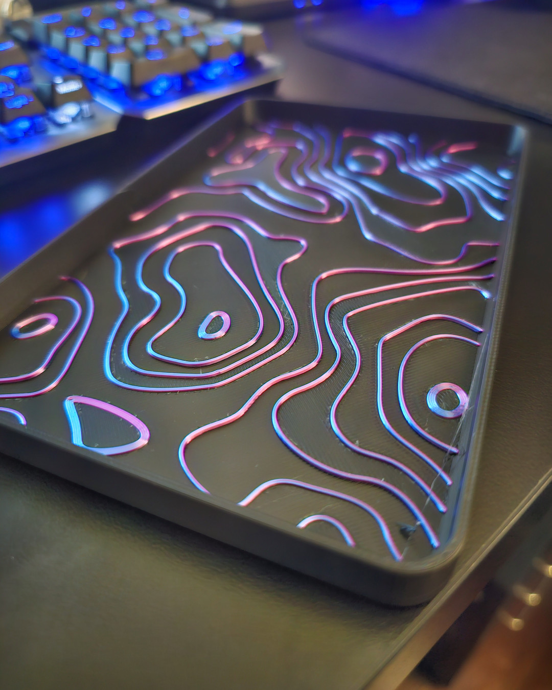 A backlit topographic relief panel with glowing pink and blue contour lines set into a dark tray.